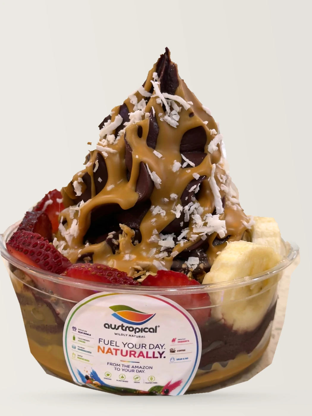 A tall açaí swirl under caramel sauce and shredded coconut, with strawberries and banana.